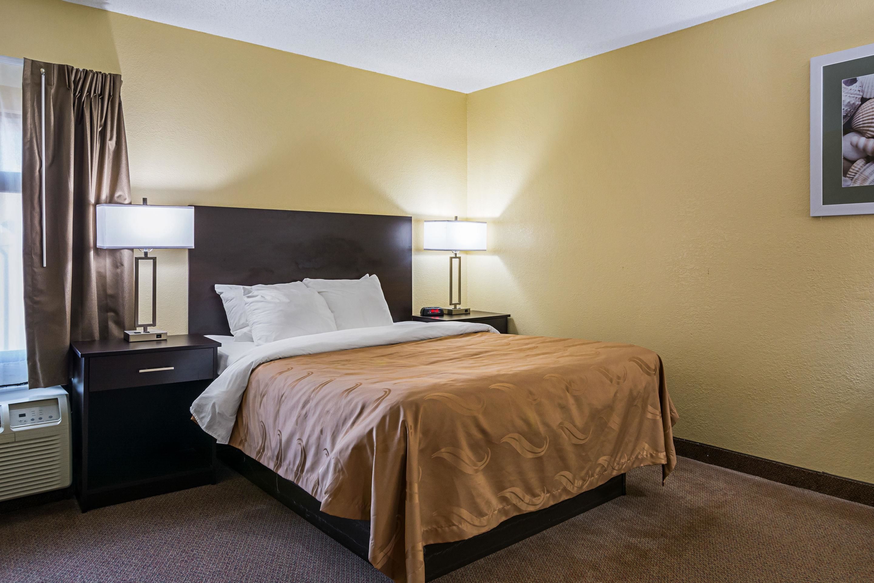 A hotel room with a bed, two bedside tables with lamps, a heater, and a framed picture on the wall.