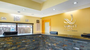 A reception area with a stone counter, a reception desk, and a wall with the hotel name and amenities. - Quality Inn & Suites Greensburg I-74 (Greensburg)