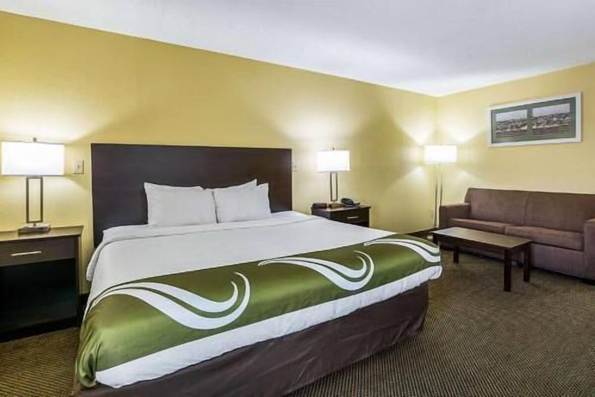 Una habitació d'hotel amb un llit, una tauleta de nit, una làmpada, un sofà i un quadre a la paret.