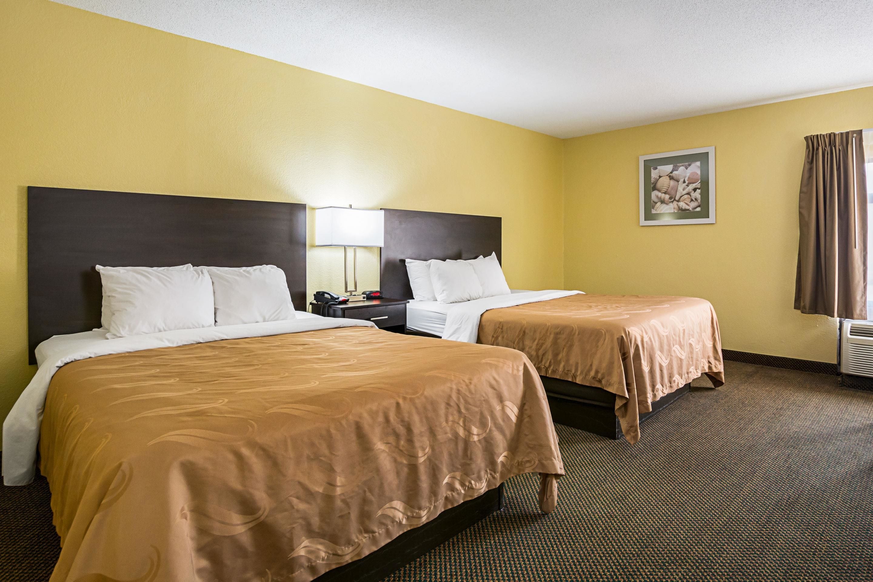 A hotel room with two beds, a nightstand, a lamp, and a framed picture on the wall.