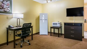 A hotel room with a desk, chair, refrigerator, microwave, TV, and a dresser. - Quality Inn & Suites Greensburg I-74 (Greensburg)