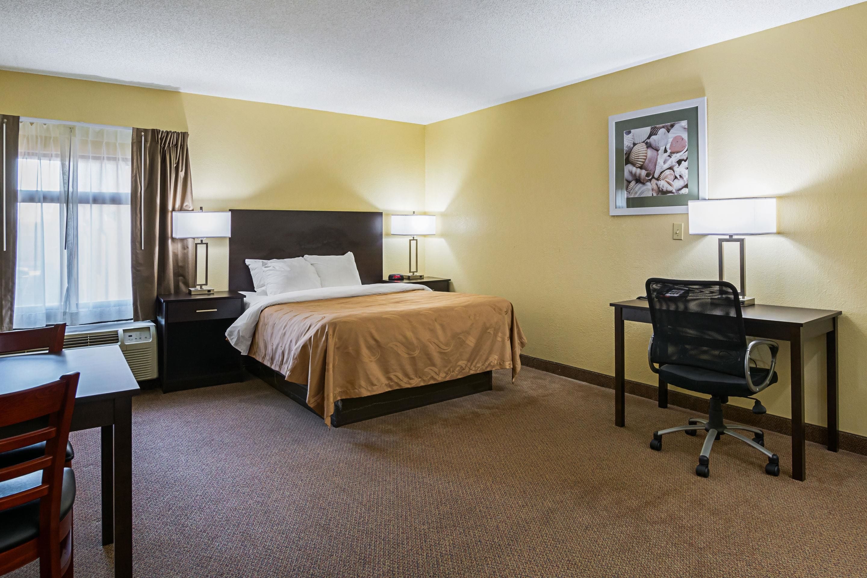 A hotel room with a bed, desk, chair, and two bedside lamps.