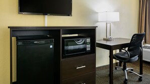 A hotel room with a flat-screen TV mounted on the wall, a desk with a lamp, a black office chair, and a minibar. - Quality Inn & Suites Greensburg I-74 (Greensburg)