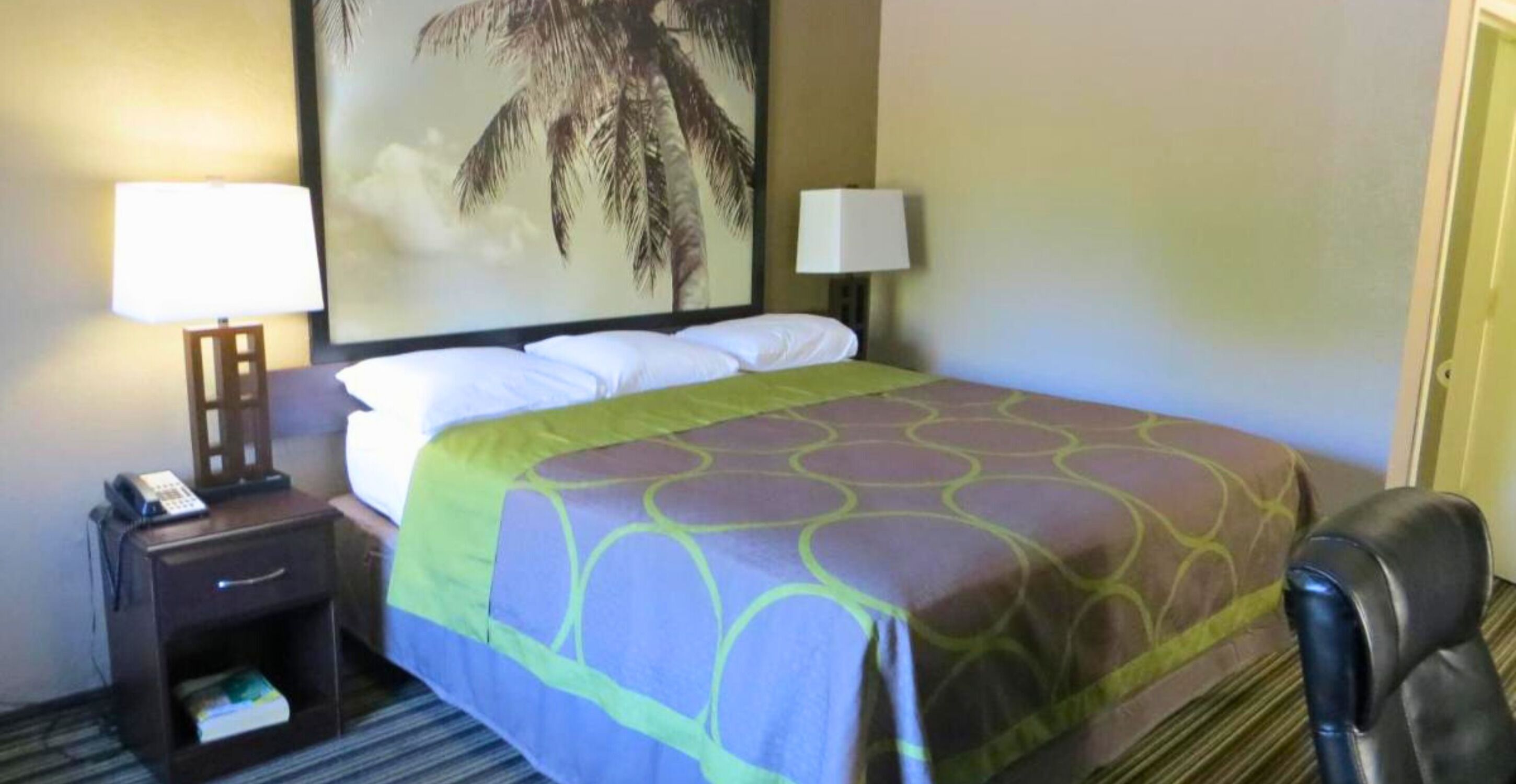 Camera d'albergo con un letto, due abat-jour, un comodino con il telefono, una poltrona e un grande quadro appeso al muro.