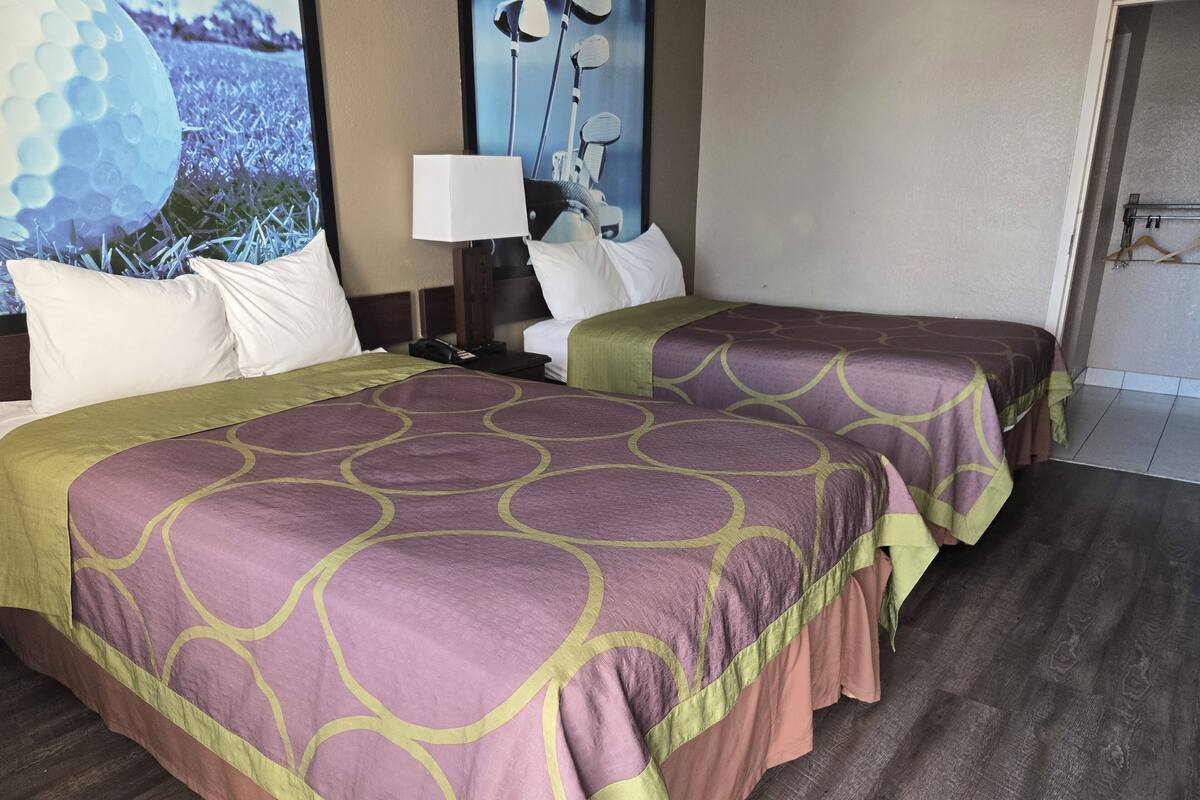 A hotel room with two beds, a nightstand, a lamp, and a view of a golf course.