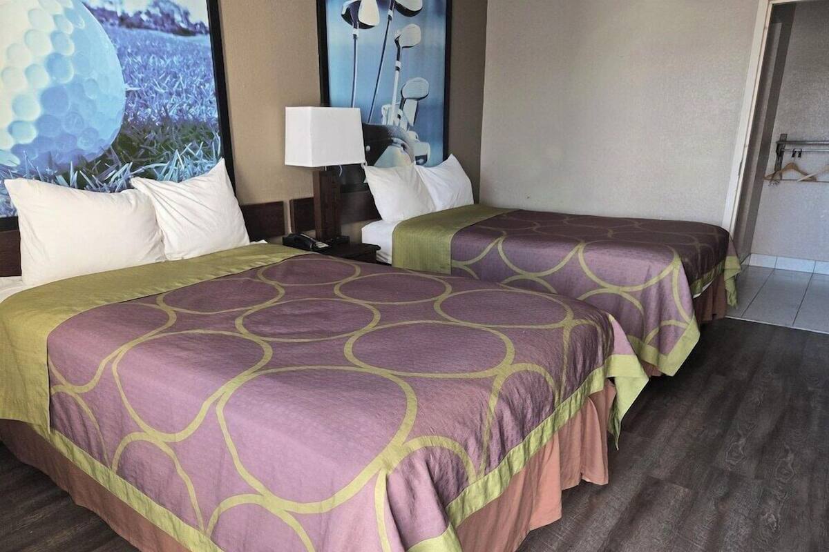 A hotel room with two beds, a nightstand, a lamp, and a view of the outdoors.