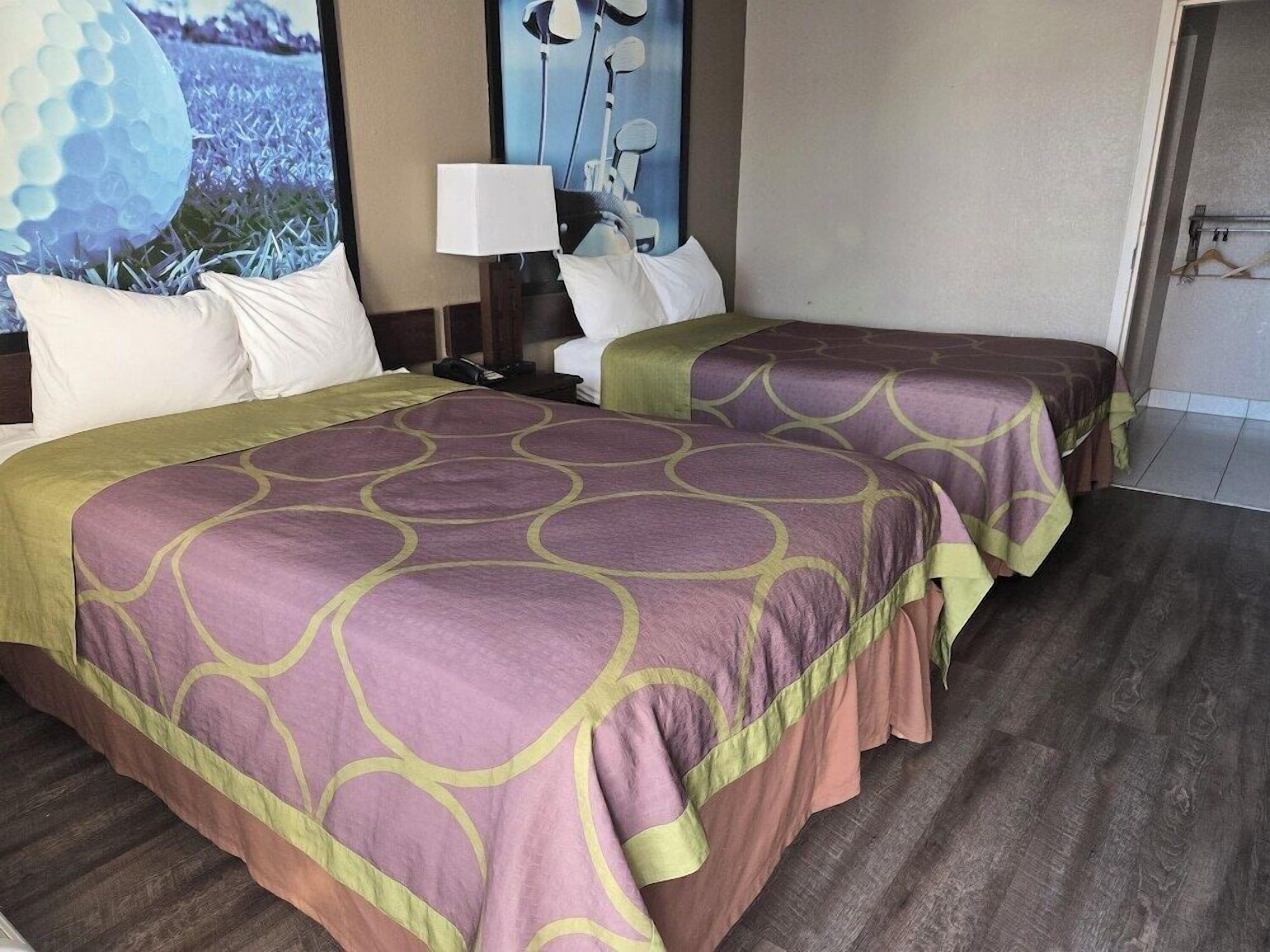 A hotel room with two beds, a nightstand, a lamp, and a view of the outdoors.