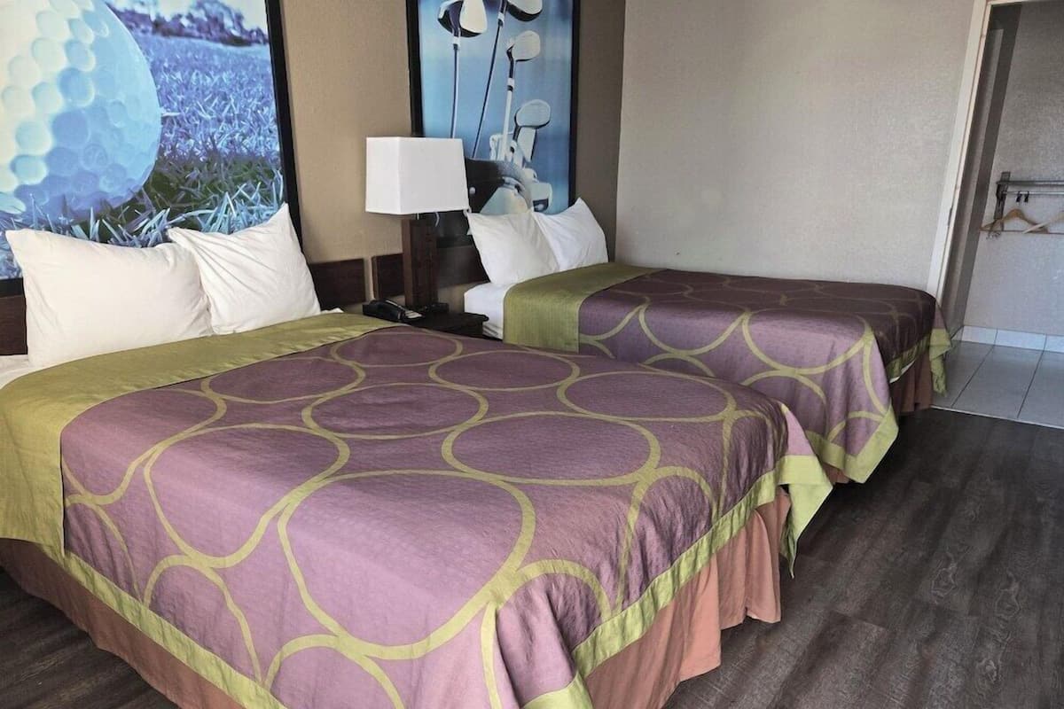 A hotel room with two beds, a nightstand, a lamp, and a view of the outdoors.