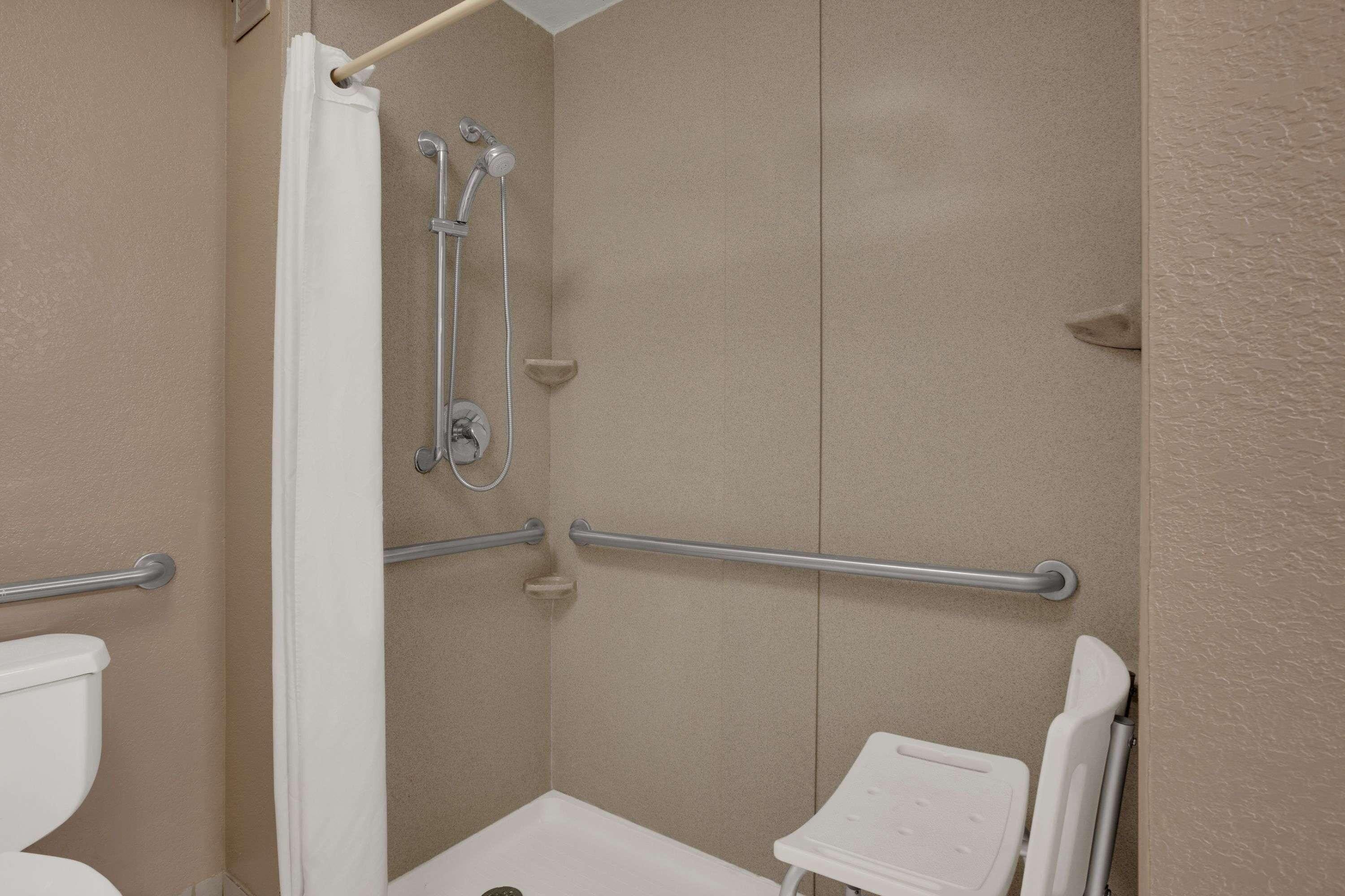 Een badkamer met een douche, toilet en handgrepen.