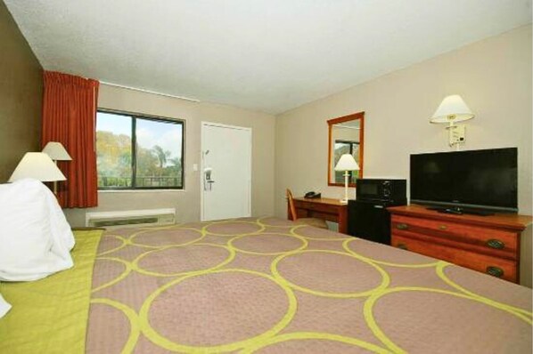 Habitación de hotel con cama, escritorio con televisor, silla, cómoda y ventana con cortinas.