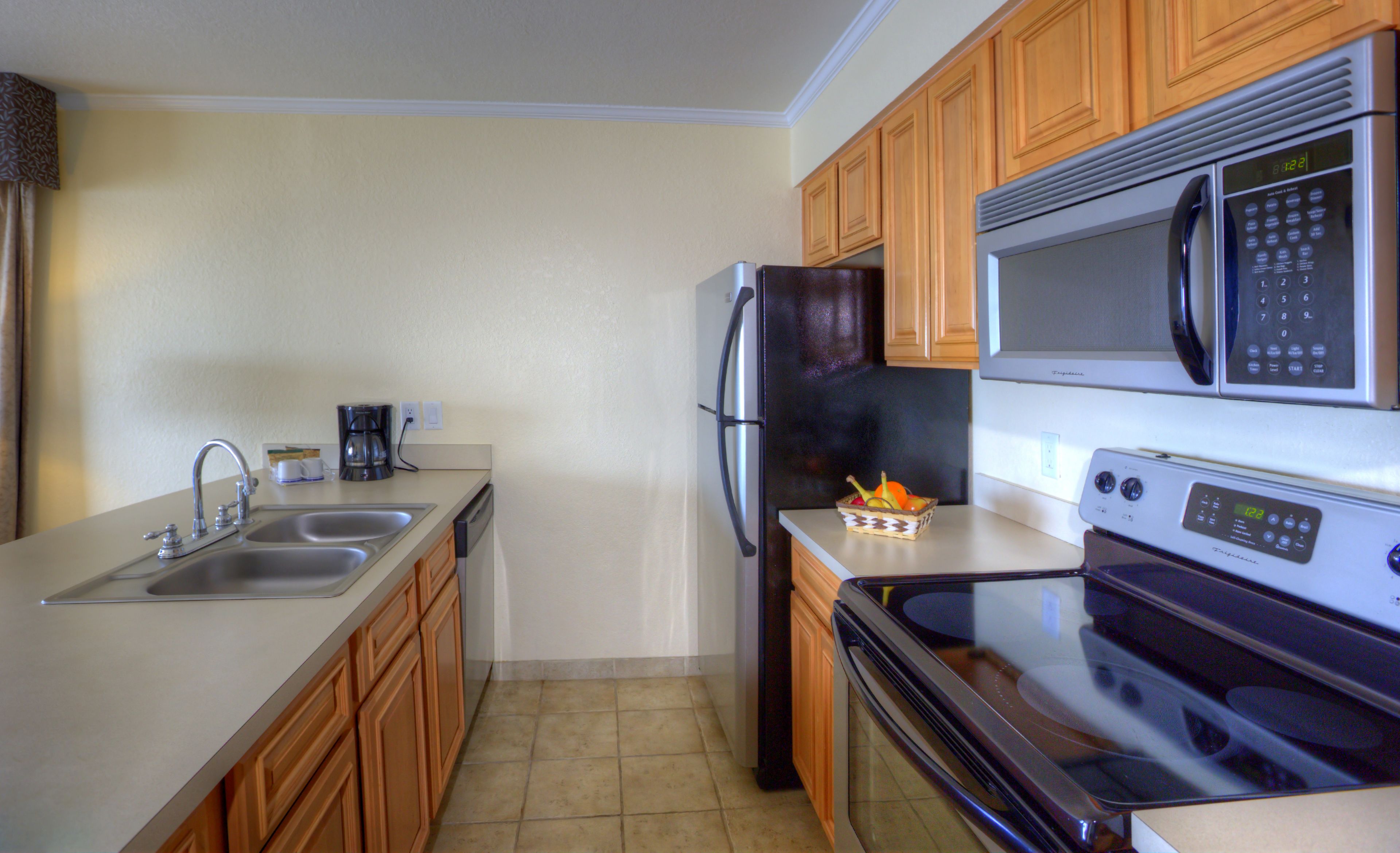 A kitchen with wooden cabinets, stainless steel appliances, a coffee maker, and a fruit basket.
