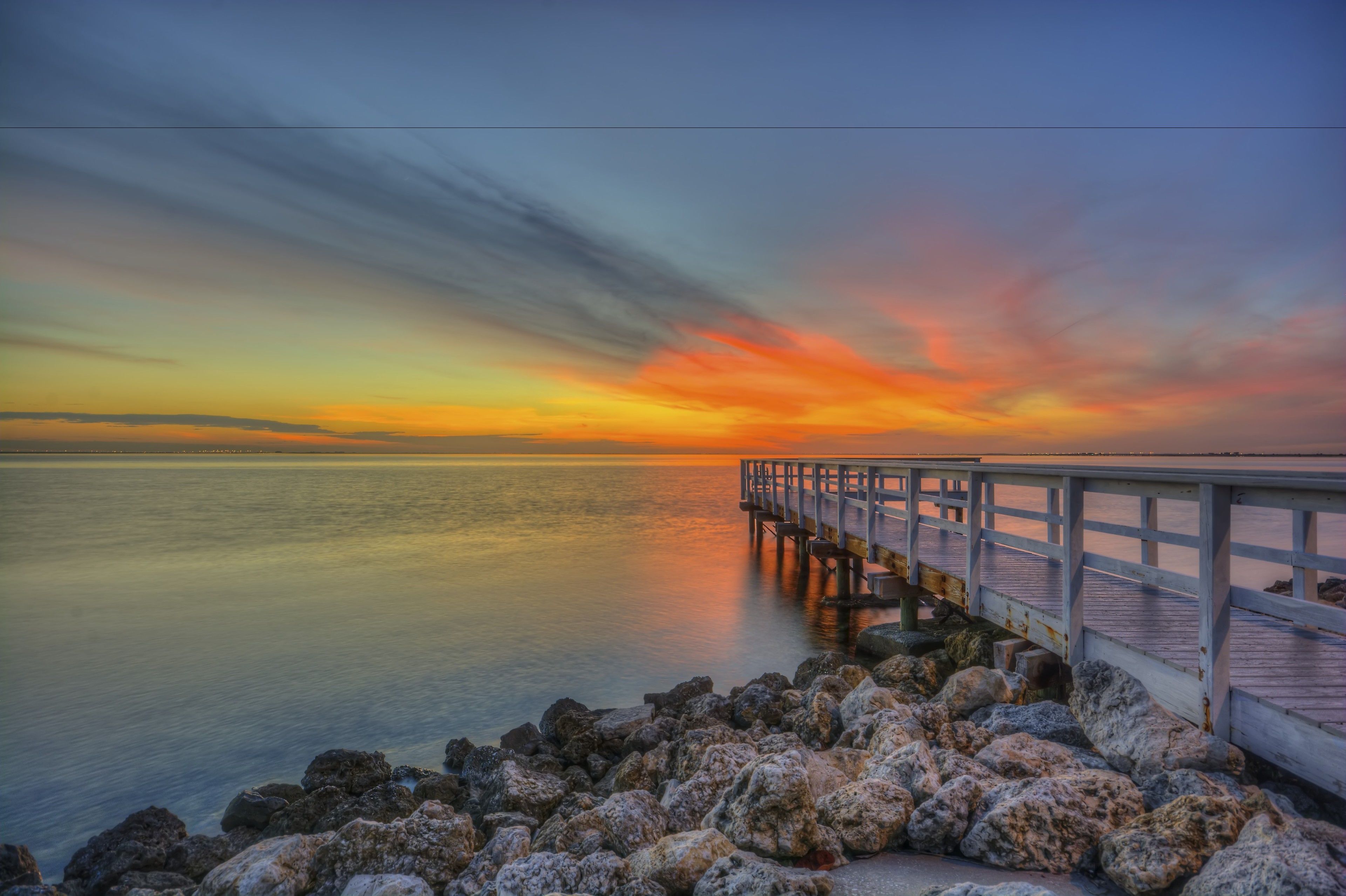 A pier extending into calm water with a sunset in the background.