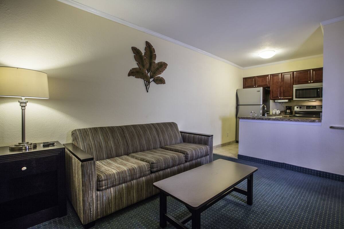 A compact living space with a sofa, a small table, a lamp, and a kitchenette area.