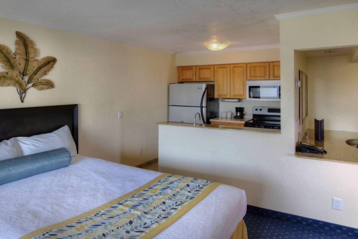 A hotel room with a bed, a small kitchenette, and a decorative wall piece.