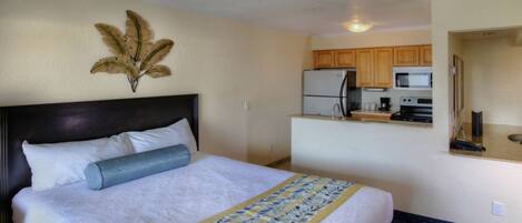 A hotel room with a bed, a small kitchenette, and a decorative wall piece.