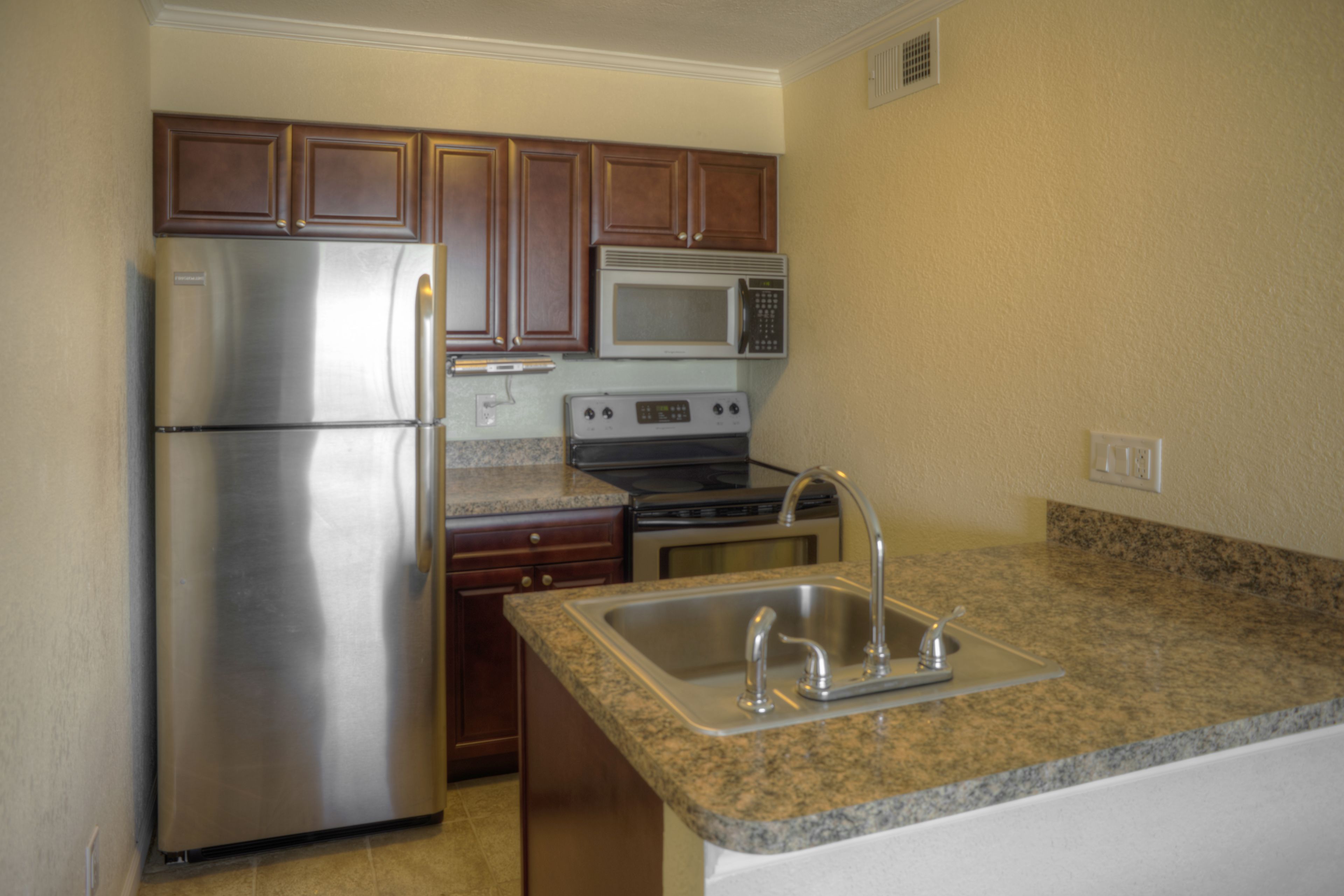A kitchen with stainless steel appliances, wooden cabinets, granite countertops, and a double sink.