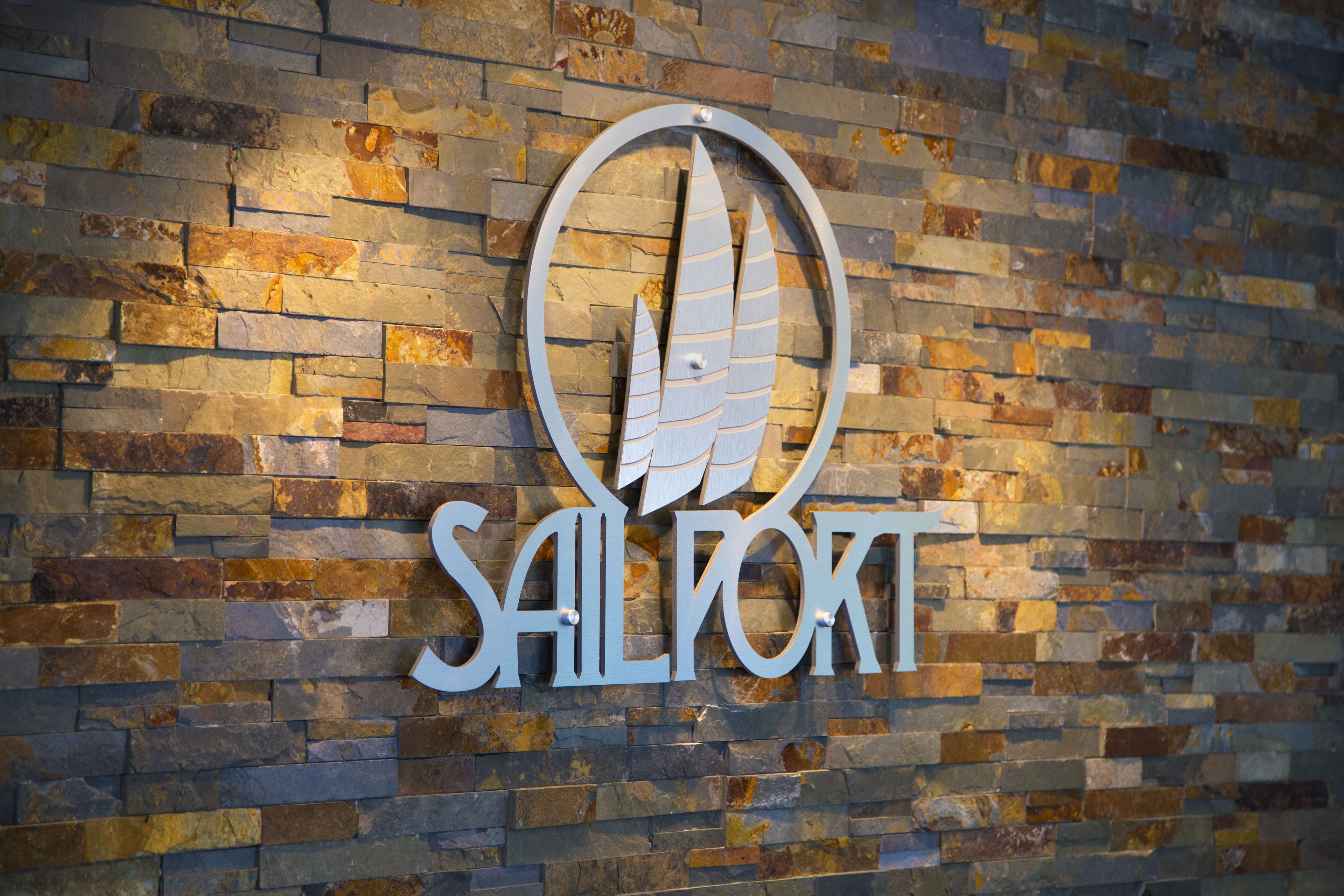 A sign with the word "SAILPORT" and a stylized bird design on a stone wall.
