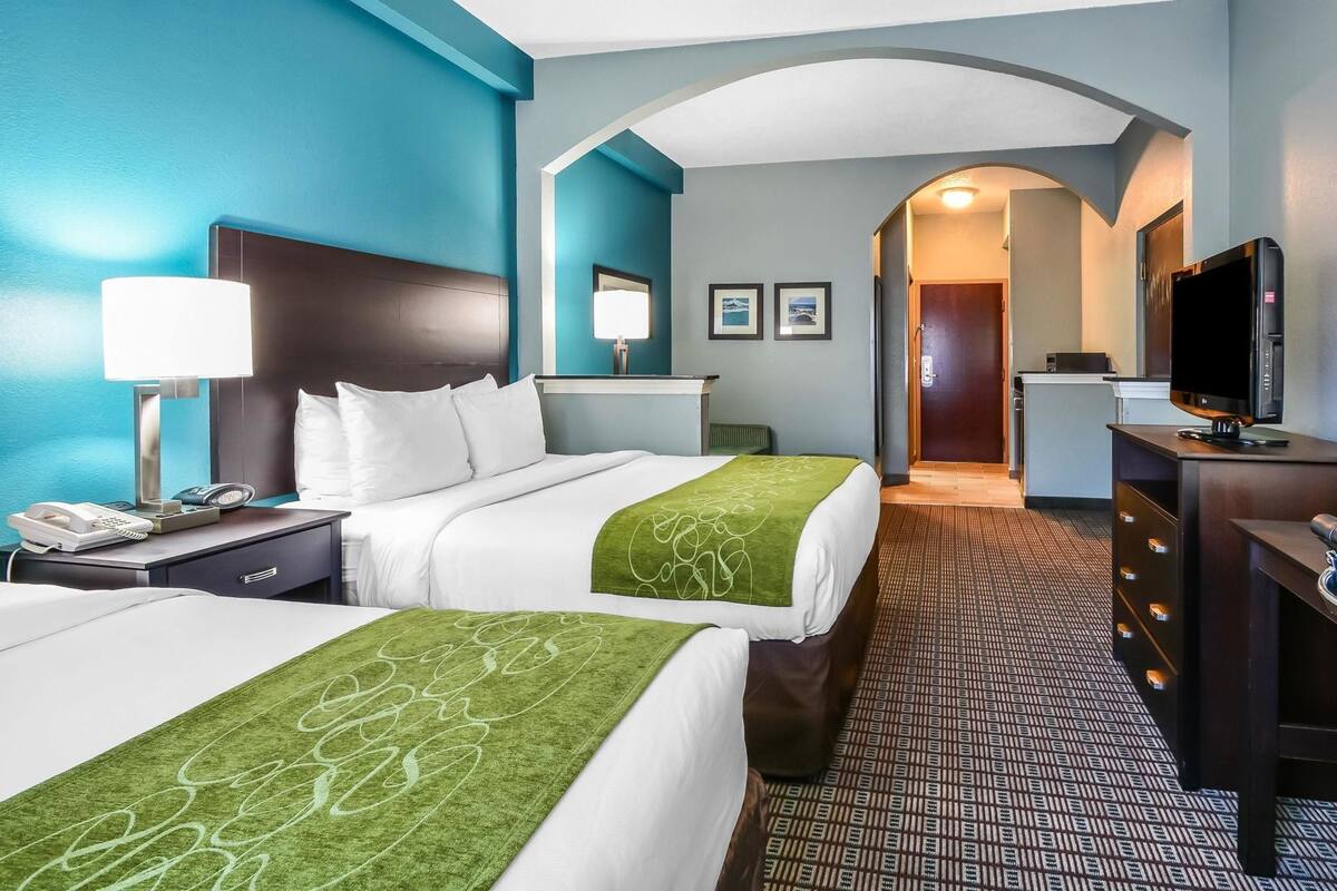 Une chambre d’hôtel avec deux lits, un bureau, une télévision et une salle de bain visible à travers une arche.