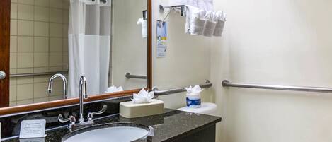 Un baño con lavamanos, espejo, toallero y retrete.