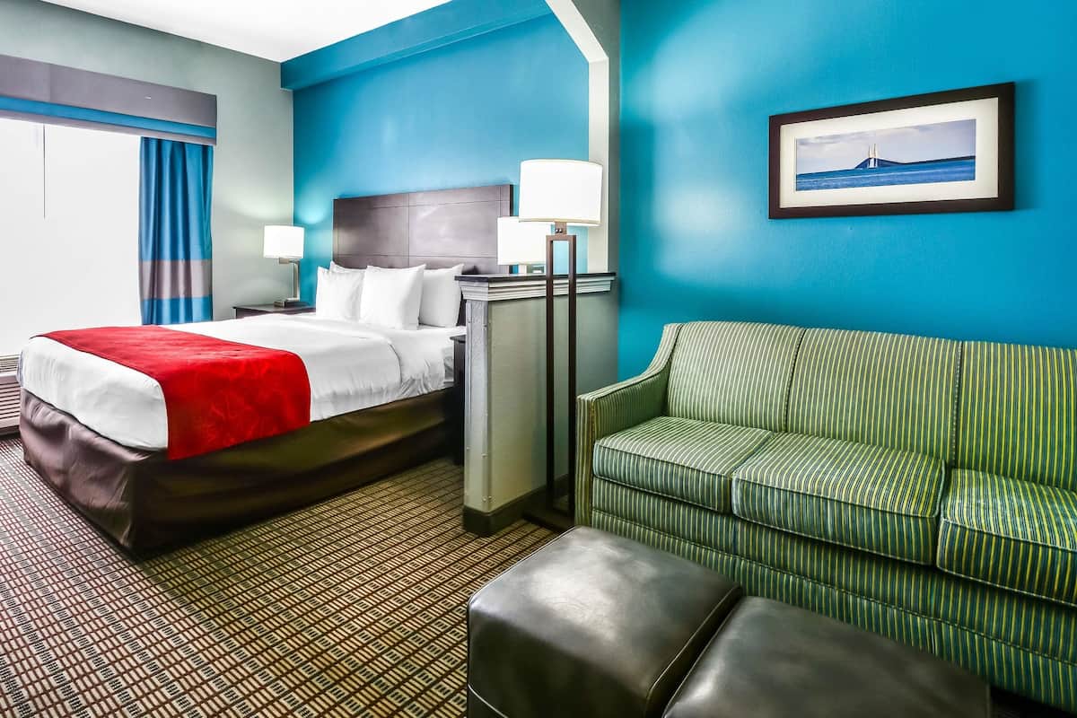 Une chambre d’hôtel avec un lit, un canapé à rayures vertes, une couvre-lit rouge et blanche, un sol à motifs et un tableau encadré au mur.
