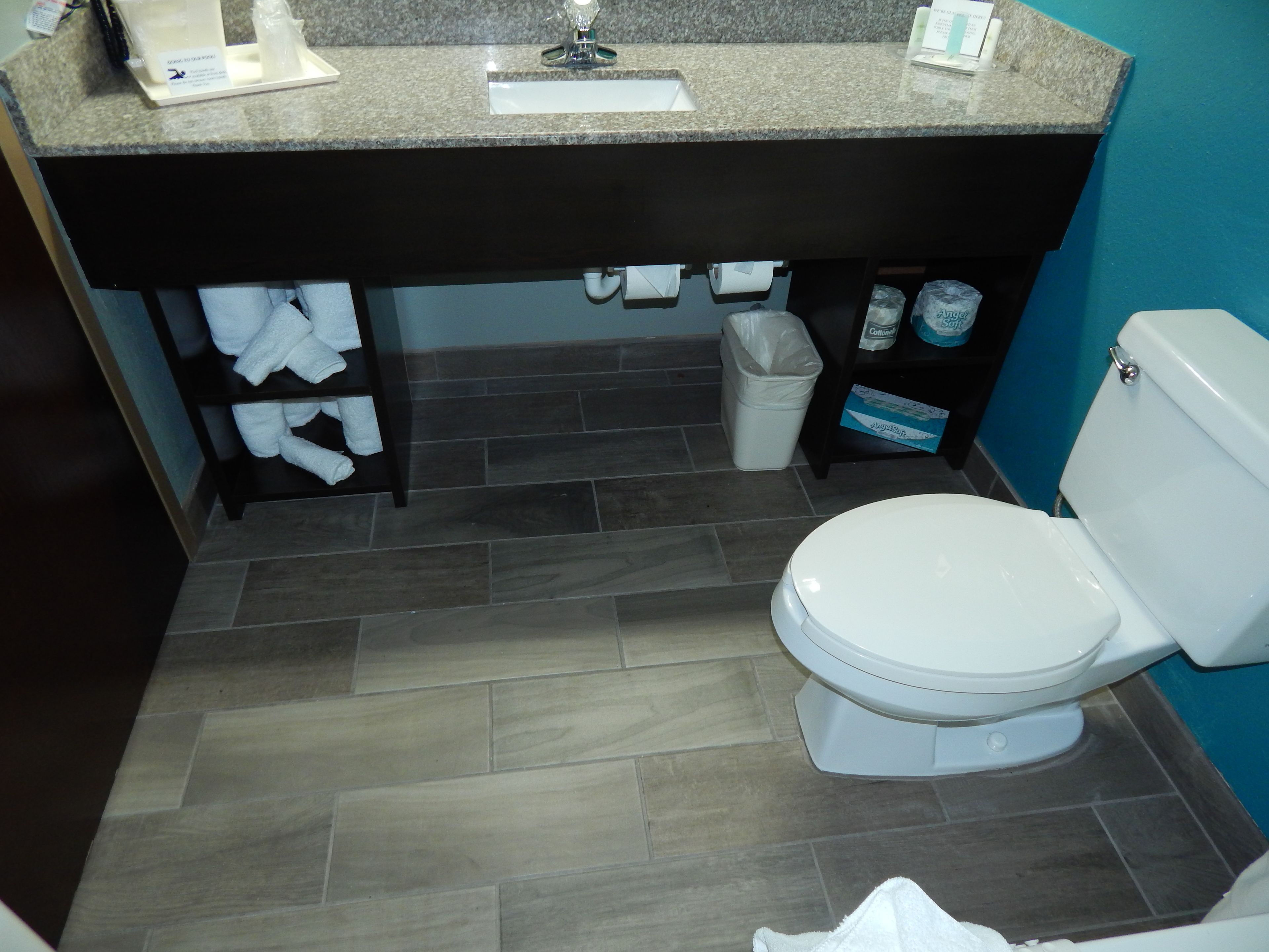 A bathroom with a white toilet, a sink with a granite countertop, and a shelf with towels and toiletries.