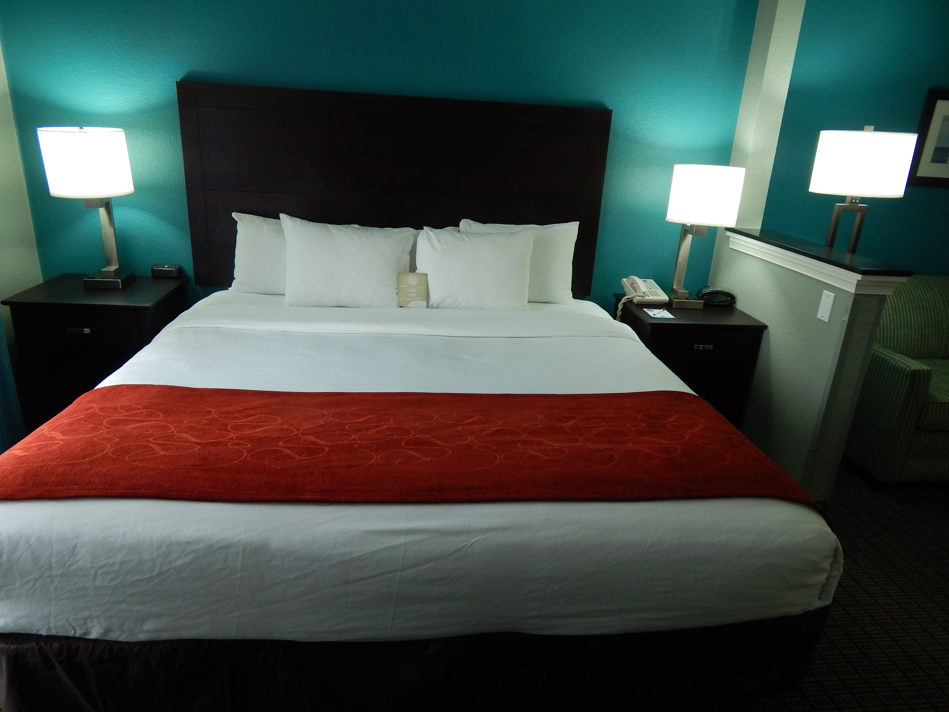 A hotel room with a large bed, two bedside tables, a nightstand, and a green chair.