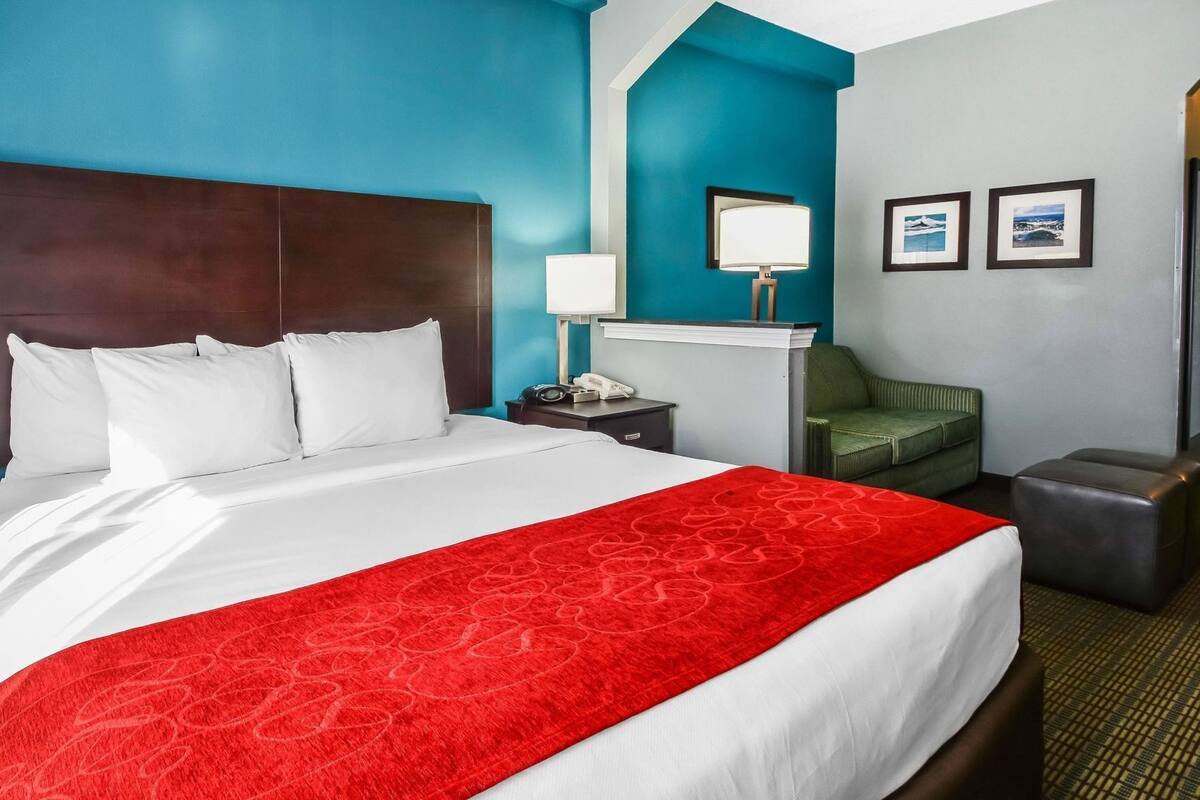 Une chambre d’hôtel avec un grand lit, un bureau, une chaise verte et un tapis rouge qui apporte une touche de couleur.
