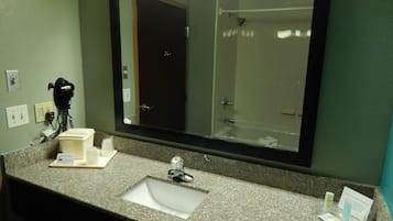 Un baño con encimera de granito, lavabo, espejo, secador de pelo y artículos de aseo.