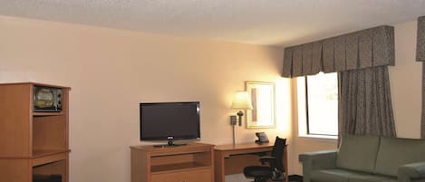 A hotel room with a bed, a desk with a television, a chair, a lamp, and a window with curtains.