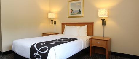 A hotel room with a bed, two bedside tables, a nightstand, a lamp, and a painting on the wall.
