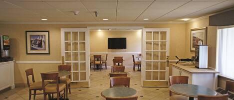 A hotel lobby with multiple seating areas, a television mounted on the wall, and a window providing natural light.