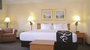 A hotel room with a large bed, two bedside lamps, a chair, a nightstand, and two framed pictures on the wall. - La Quinta Inn & Suites by Wyndham Tampa Fairgrounds - Casino (Tampa)