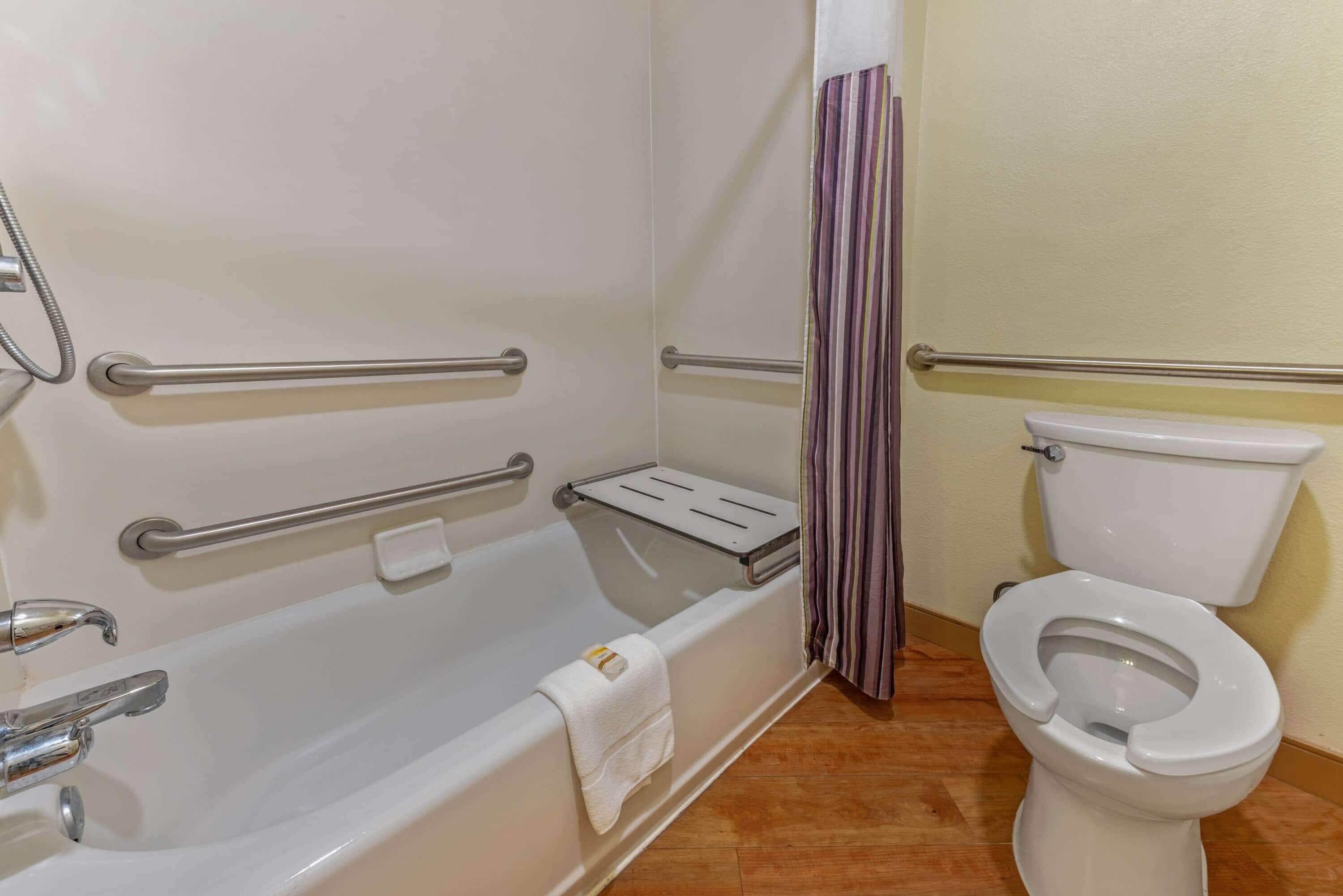 Un baño con bañera, barras de apoyo, inodoro y cortina de ducha.