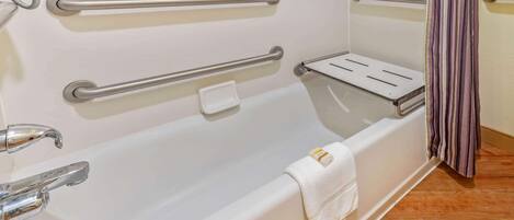 Une salle de bain avec une baignoire blanche, des barres d’appui, une douchette à main, un porte-serviettes et un rideau de douche à rayures.