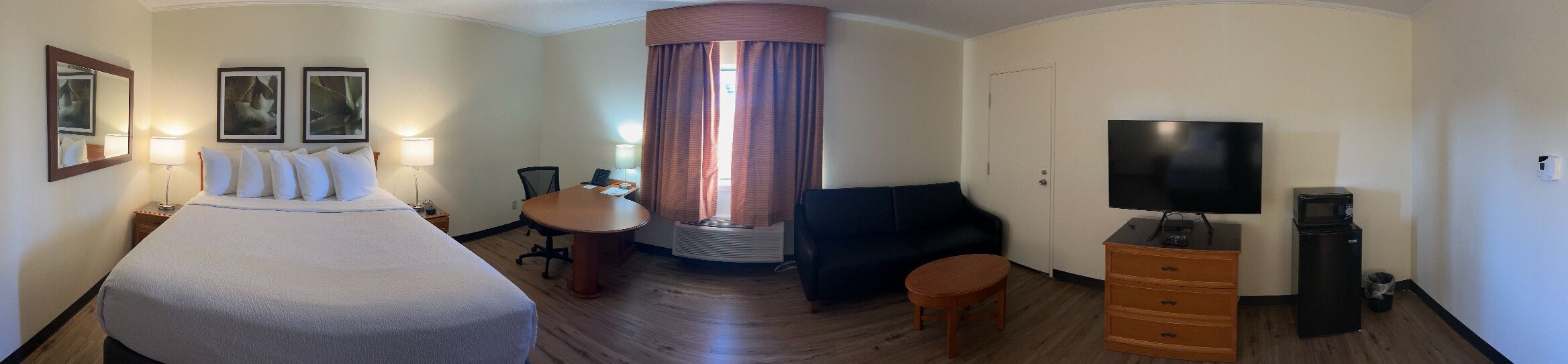 A hotel room with a large bed, a desk, a chair, a TV, and a dresser.