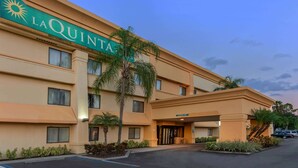 Un hotel de varios pisos con un llamativo letrero 'LAQUINTA', una entrada cubierta y un área de estacionamiento.