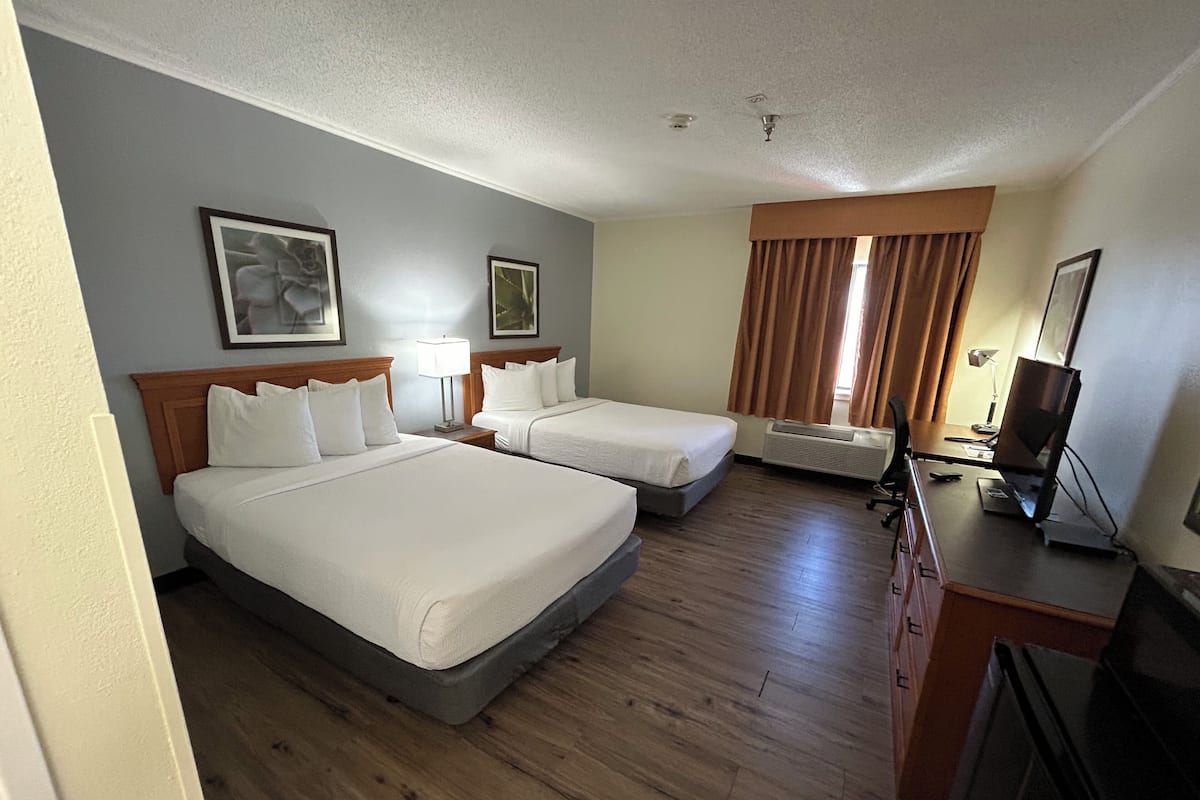 A hotel room with two beds, a desk, a TV, and a window with curtains.