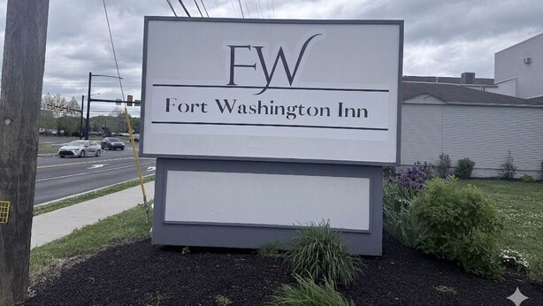 A sign for Fort Washington Inn with a clear view of the road and a building in the background.