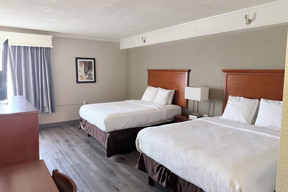 A hotel room with two beds, a desk, a chair, and a framed picture on the wall.