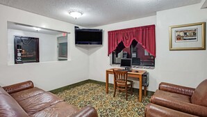 Un salón con un sofá de cuero marrón, una mesa de madera con una silla, un televisor de pantalla plana y una ventana con cortina roja.