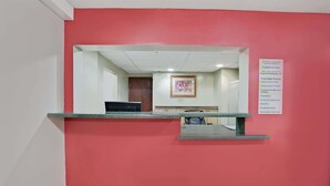 Zona de recepción con una pared roja, un mostrador de recepción y un cuadro enmarcado en la pared.