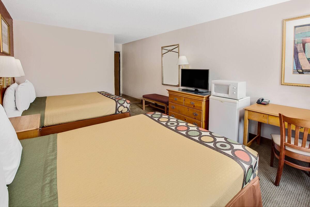Una habitació d'hotel amb dos llits, un escriptori, una televisió, una petita estanteria i un mirall.