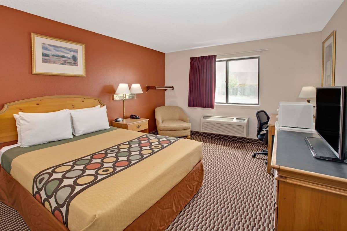 Una habitació d'hotel amb un llit, un escriptori amb un ordinador, una cadira, una finestra amb cortines i un aire condicionat fixat a la paret.