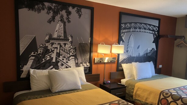 Habitación de hotel con dos camas, cada una con cubrecama estampado, una mesita de noche con lámpara y un cuadro grande enmarcados con una imagen de un puente.