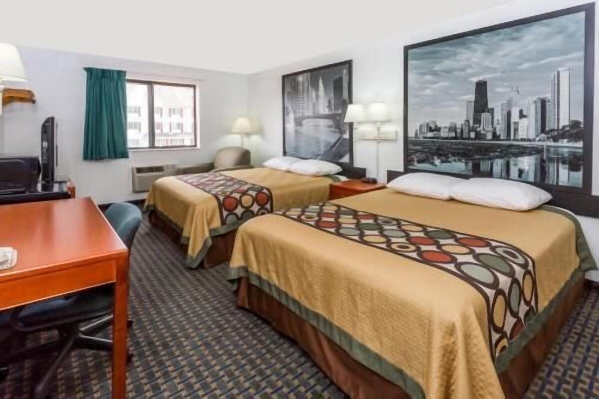 Ein Hotelzimmer mit zwei Betten, einem Schreibtisch, einem Stuhl, einem Fernseher und einem großen Stadtbild.