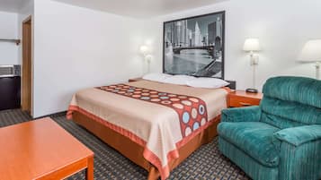 Una habitación de hotel con una cama, un sillón verde, una mesa de madera, un televisor montado en la pared y una pintura de un paisaje urbano.