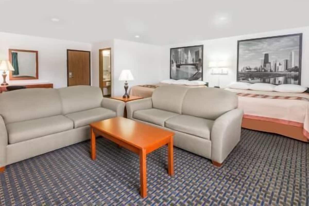 Een hotelkamer met twee banken, een klein houten tafeltje, een bed met een roze dekbed en twee wandlampen.