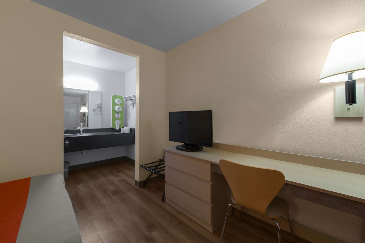 A compact hotel room with a kitchenette, a TV, a desk, and a chair.