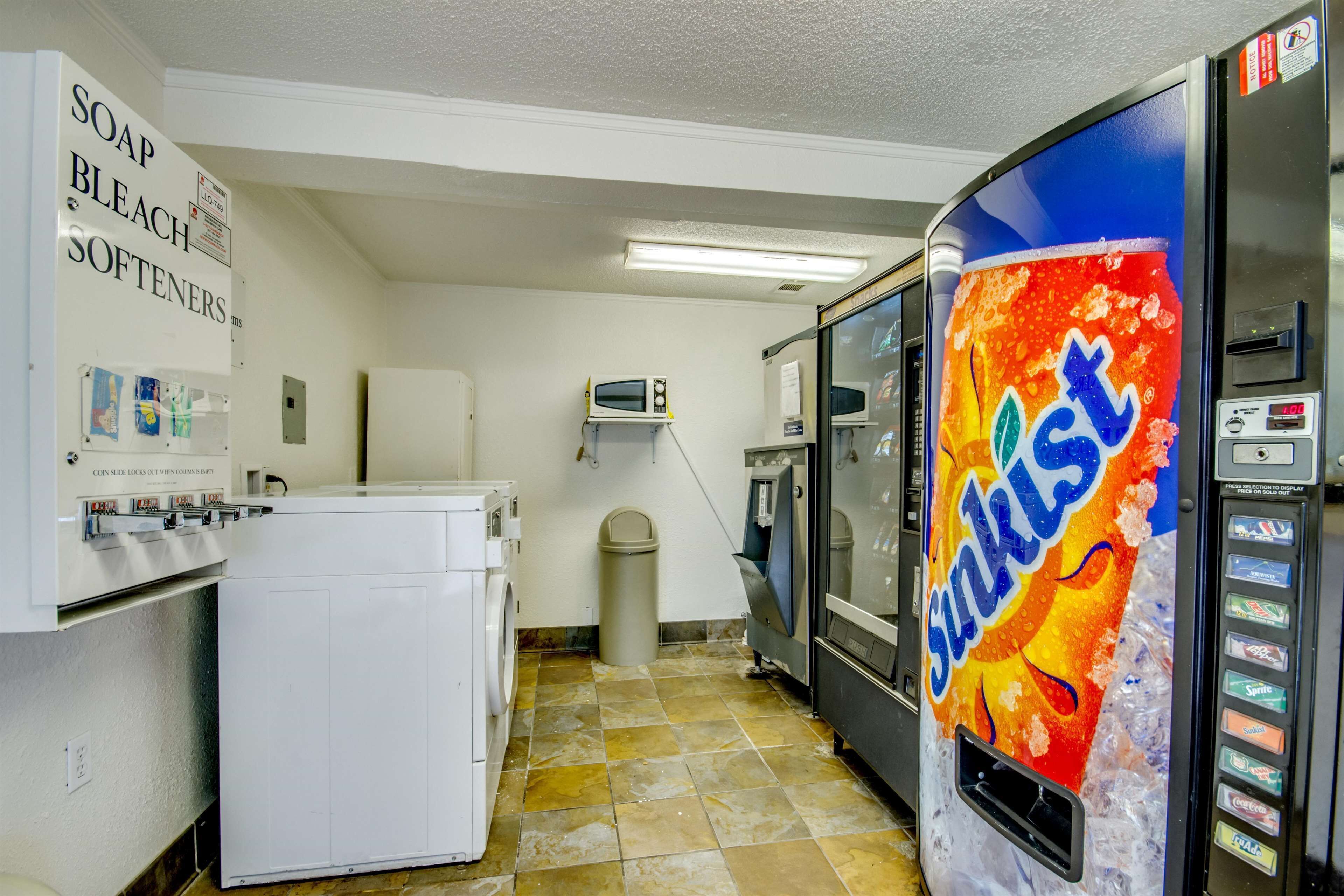 A laundry room with a washing machine, a dryer, a microwave, and a soda vending machine.