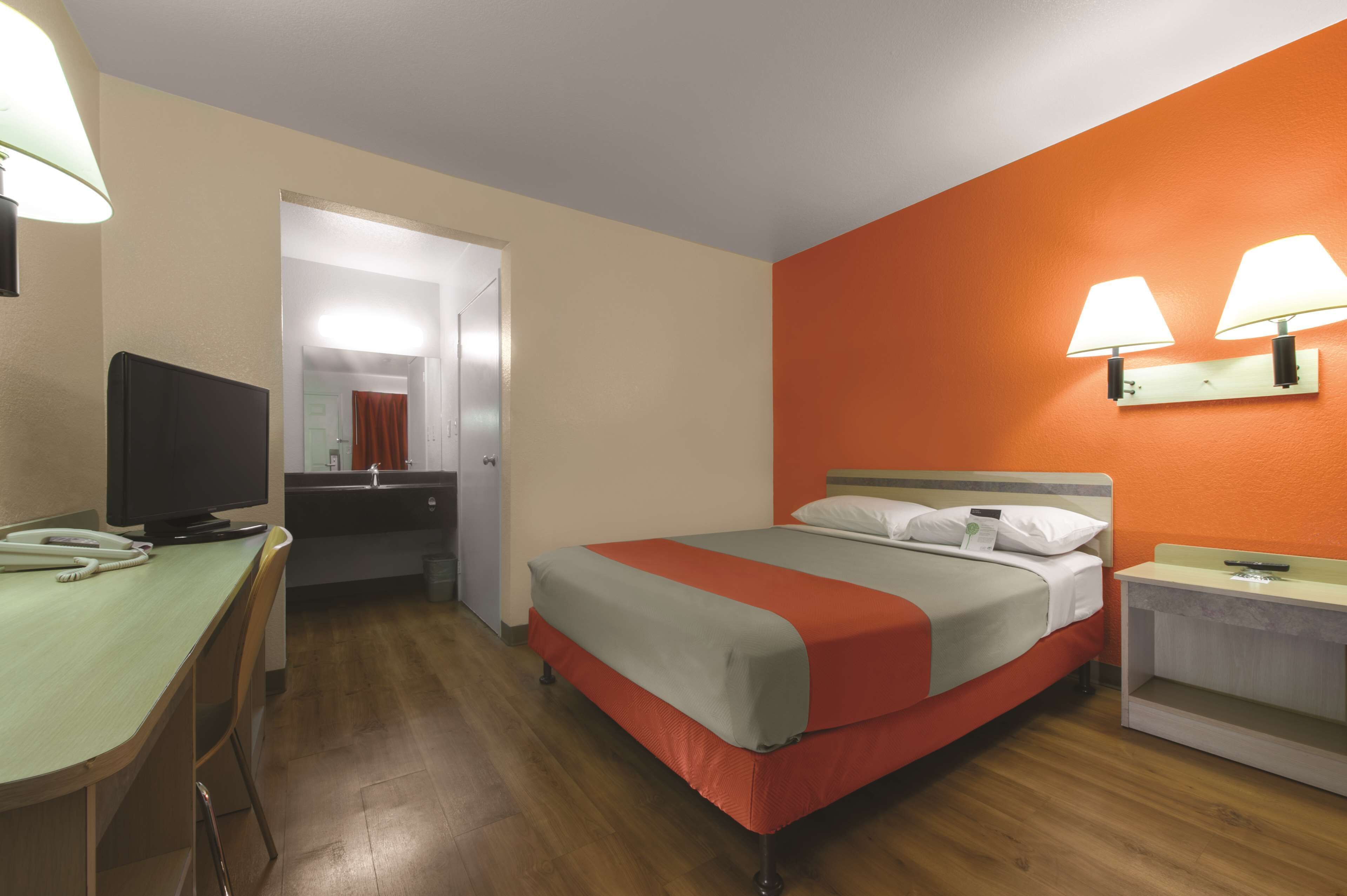 Ein Hotelzimmer mit Bett, Schreibtisch mit Computer, Fernseher und Nachttisch mit Lampe.